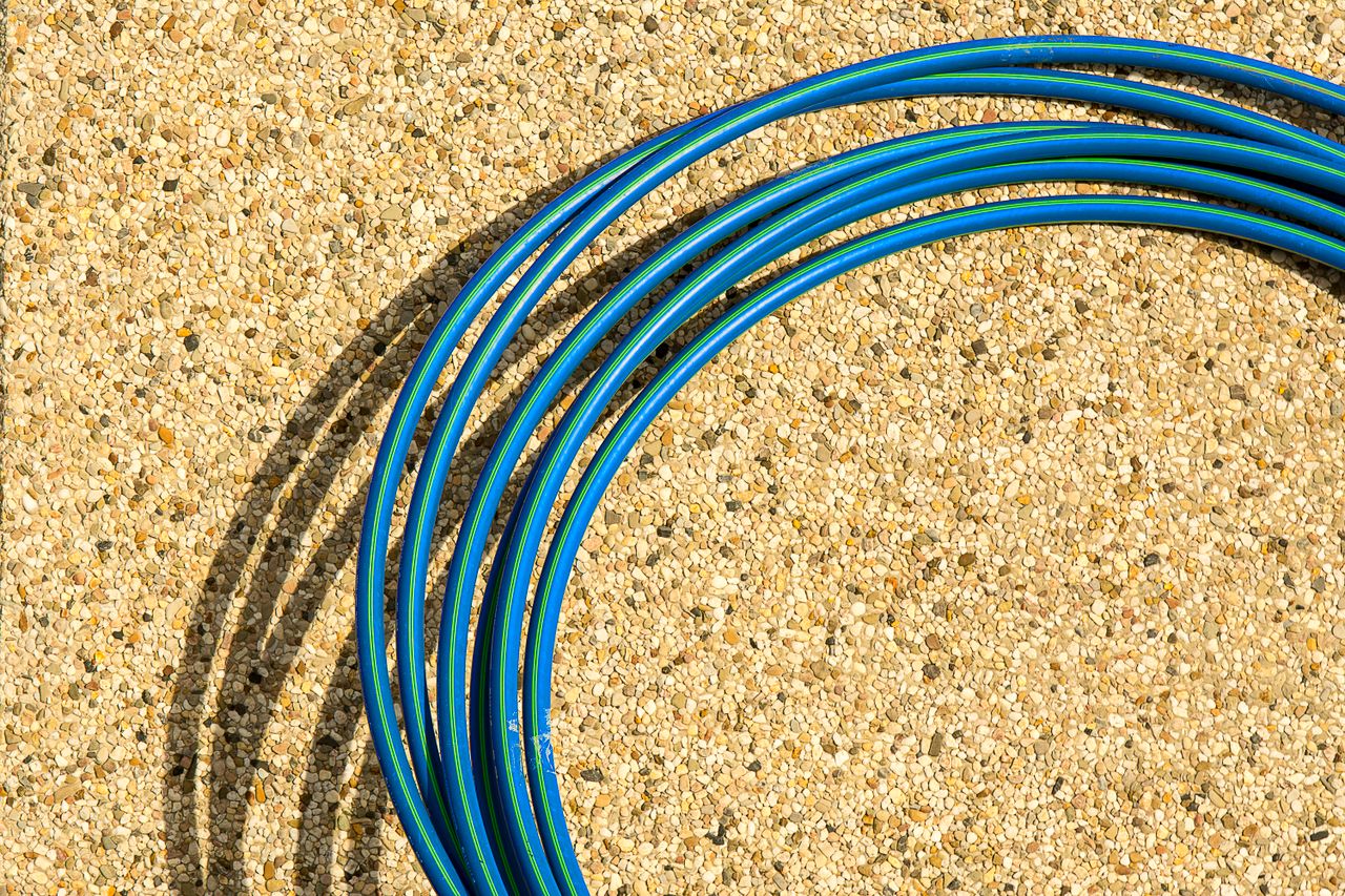 services-01 Close-up of a blue hose arranged on a textured concrete background under sunlight.